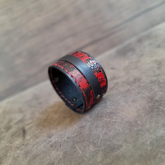 A wide black leather cuff bracelet with a red snake skin print, displayed on a wooden surface.