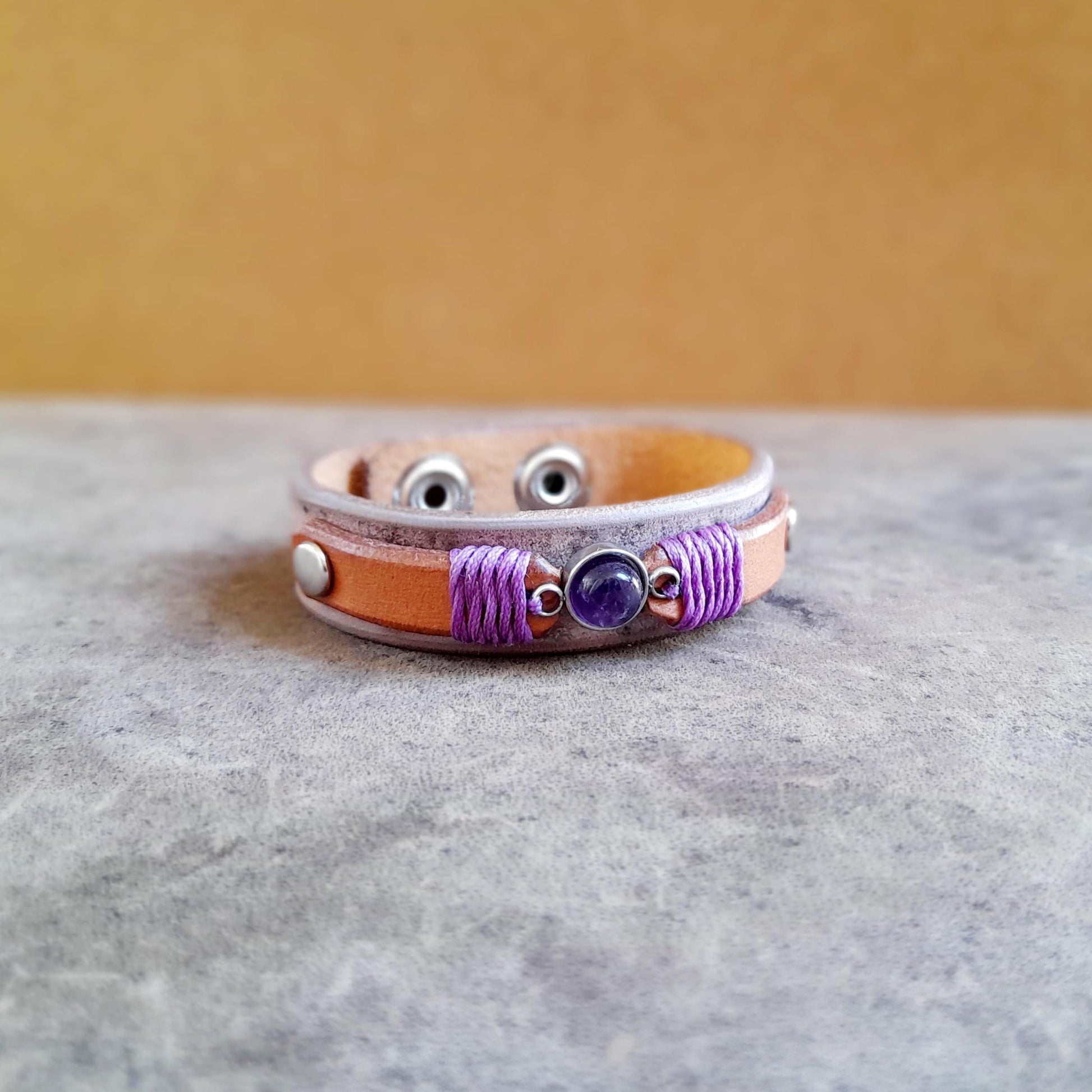 Close-up of the natural Amethyst stone on the Amethyst & Leather bracelet, showing its purple color and the purple beeswax thread detail.