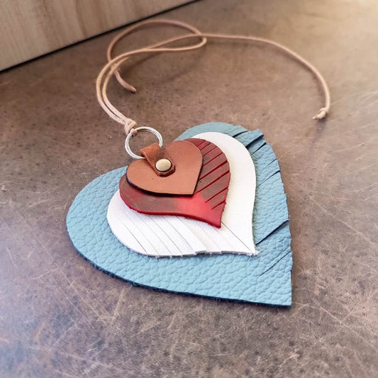 Angled view of The "Heartstrings" Charm, illustrating the depth of its four layered leather hearts, the distinct fringe patterns, and the secure leather loop and rivet attachment.