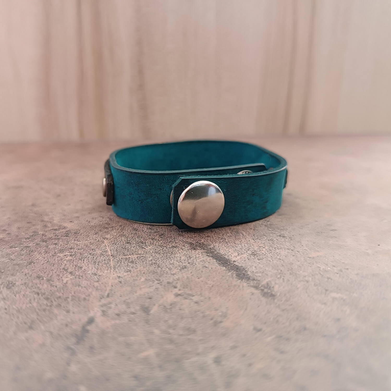 Teal leather bracelet with a silver button on a textured surface