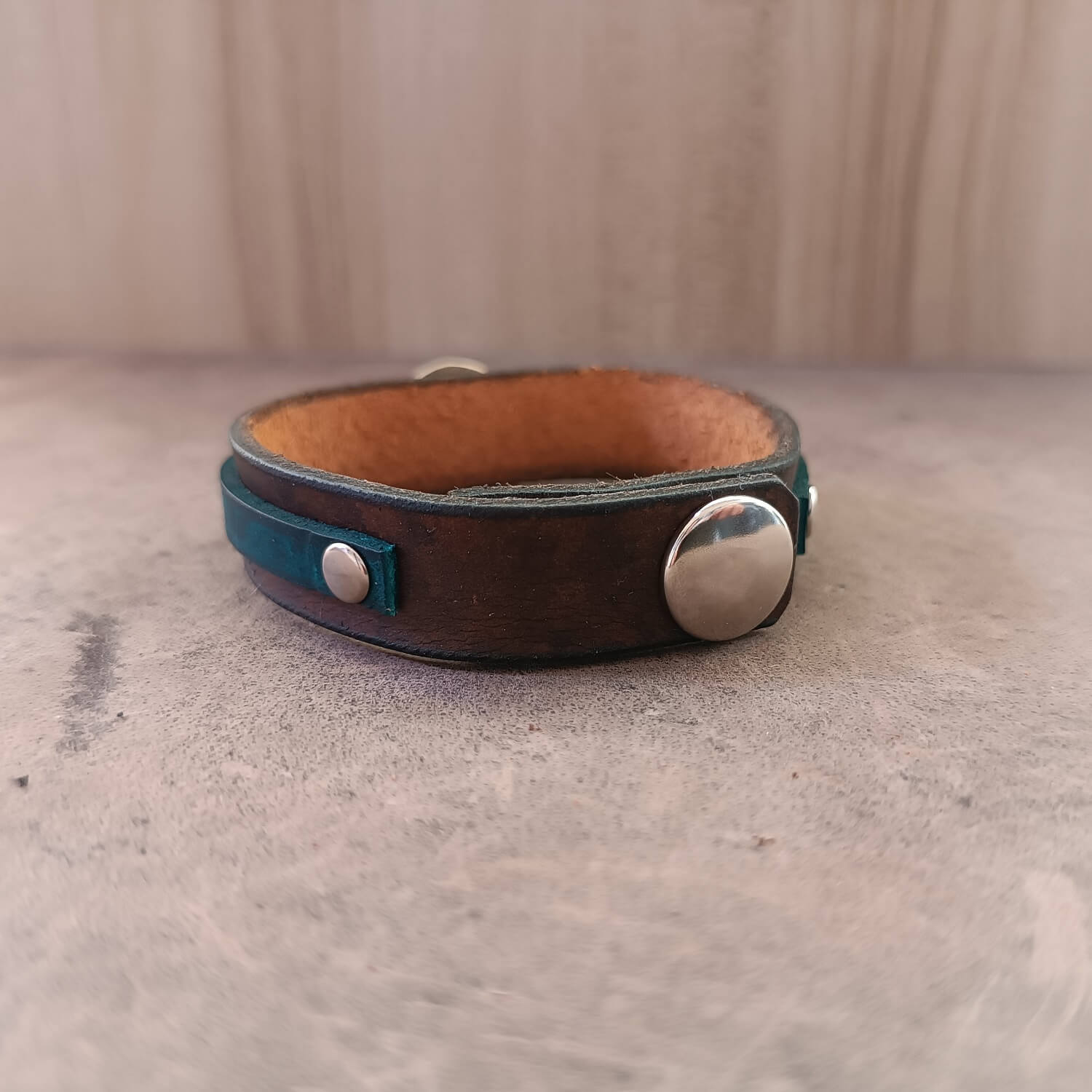 Brown leather bracelet with silver buttons on a textured surface