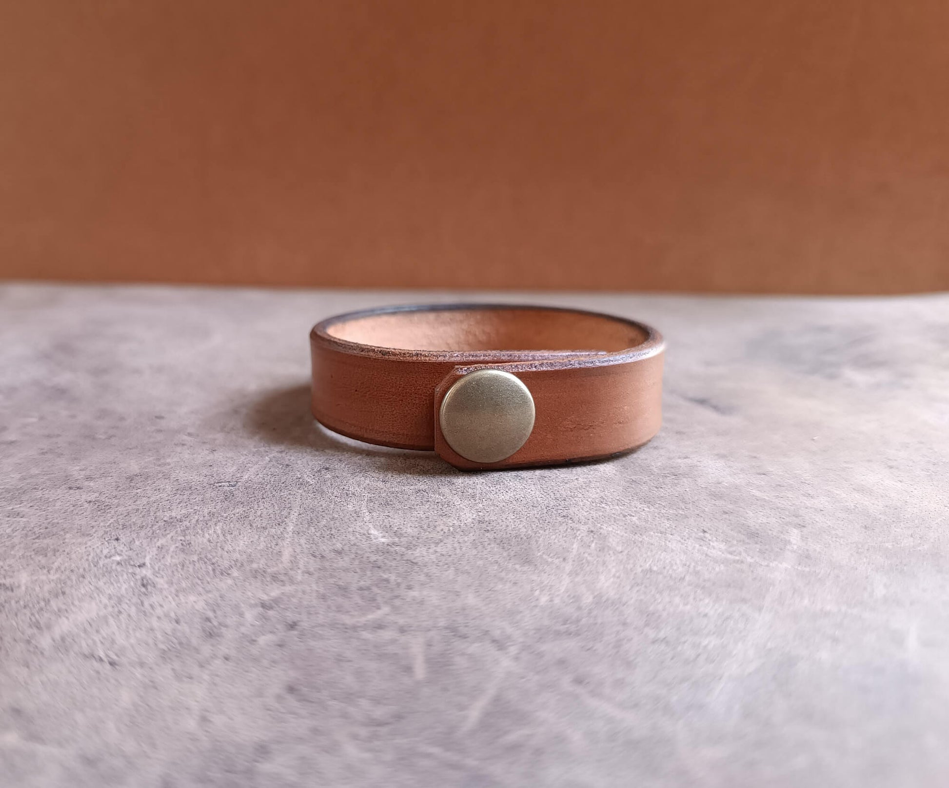 Brown leather bracelet with a silver button on a gray surface