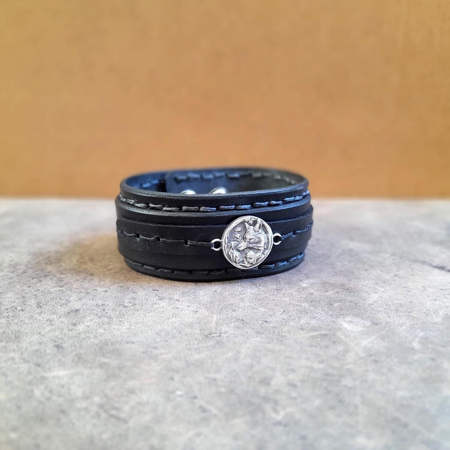 Black leather bracelet with a silver fox pendant on a gray surface