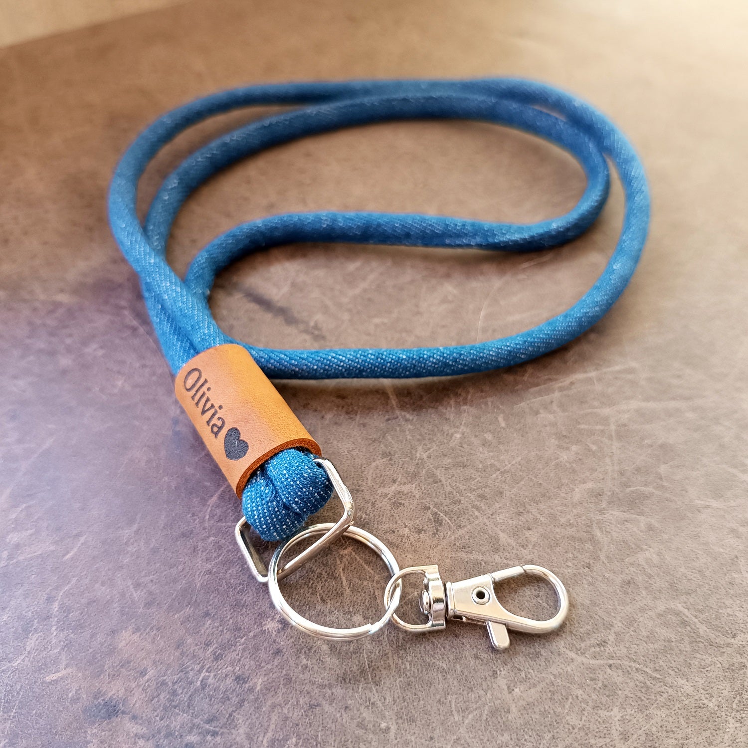 Blue denim lanyard with custom engraved leather tag and metal clip on a brown surface