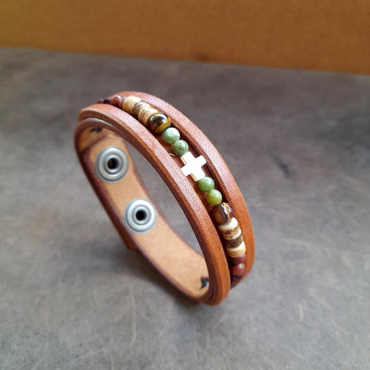 Close up οf the Boho beaded leather bracelet for men with green Jasper, Tiger's Eye, coconut beads, and an ivory cross on brown leather.