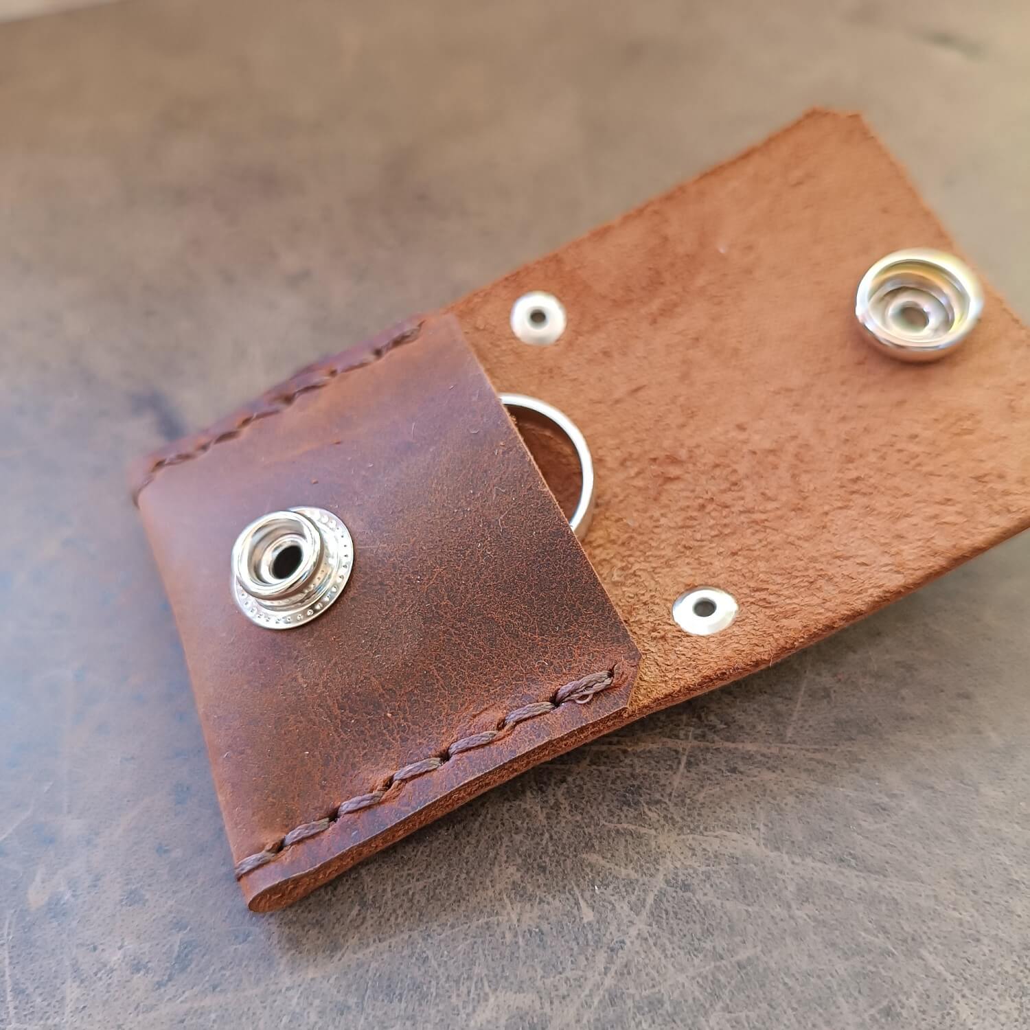 the chocolate brown ringholder keychain pouch open, showing its compact size while holding a wedding band