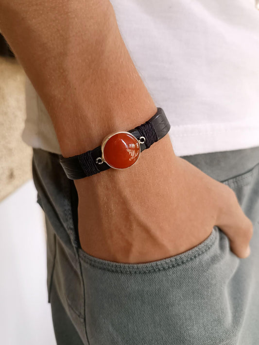 Bracelet with a red stone on a wrist, worn by a person in casual clothing.