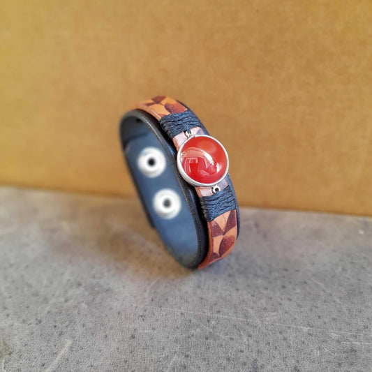 The Ember Bloom Cuff, a hand-pyrographed black and brown leather bracelet duo. Features a natural Red Carnelian gemstone set in a sterling silver pendant, with intricate burned leaf patterns.