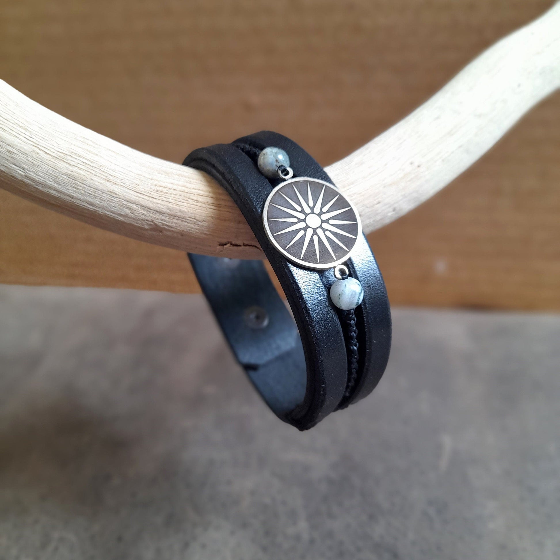 Close-up front view of Silver Vergina Sun Black Leather Bracelet, focusing on the detailed German Silver Vergina Sun charm while hanging sideways from a driftwood.