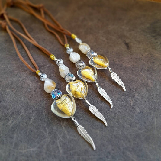 A series of boho-style car charms with natural citrine stones, yellow crystal hearts, and silver feathers, attached to brown suede cords.