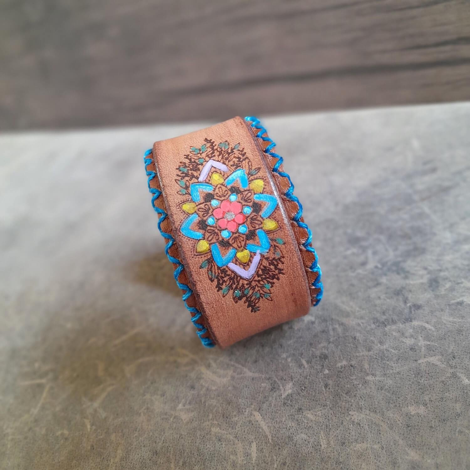 Close-up of the hand-painted mandala flower design on the bracelet, showing the vibrant colors, laser-engraved textures, and turquoise stitching.