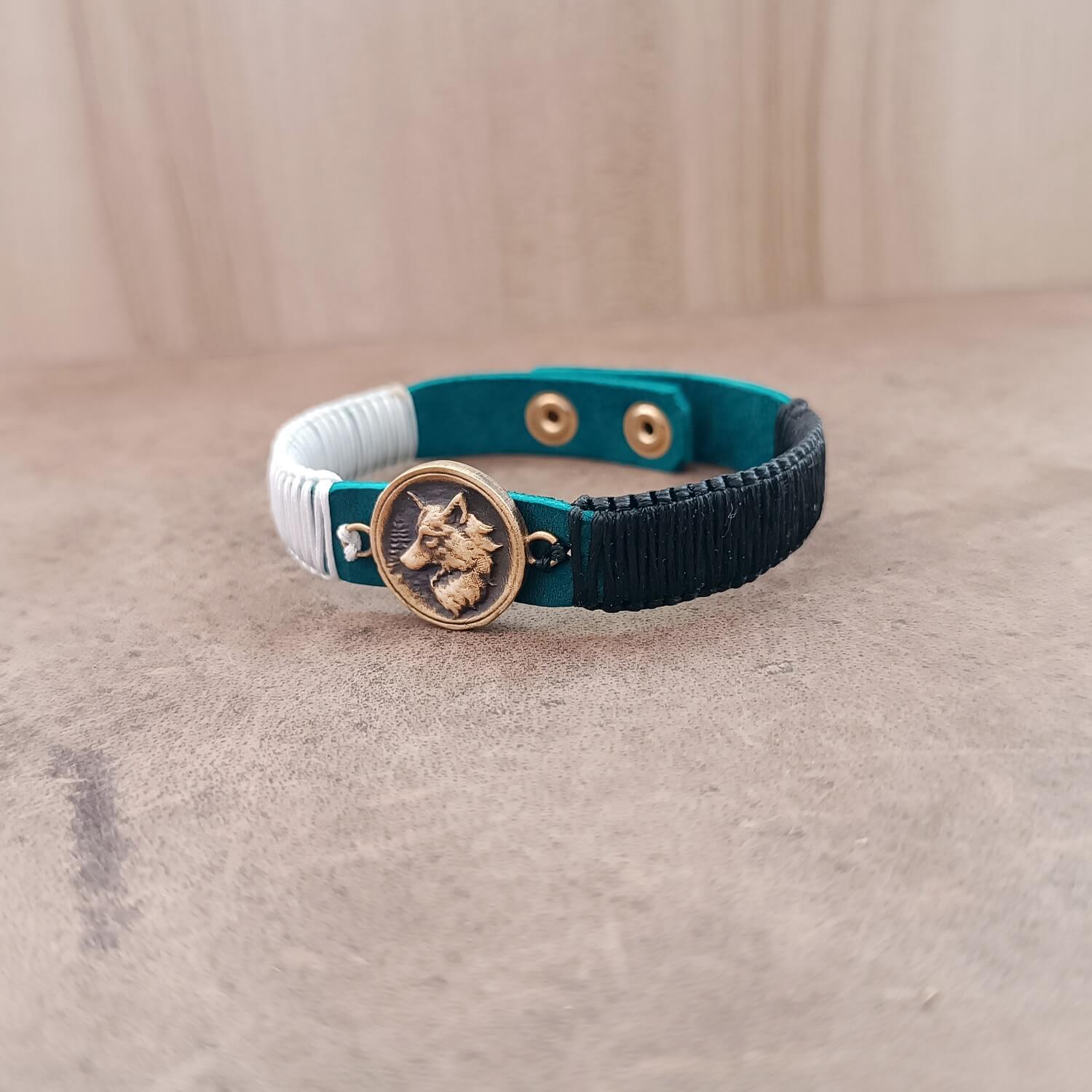 Close-up of The Instinctive Shield Wolf Bracelet, highlighting the intricate details of the oxidized brass wolf pendant and the texture of the macrame cords against the blue leather.