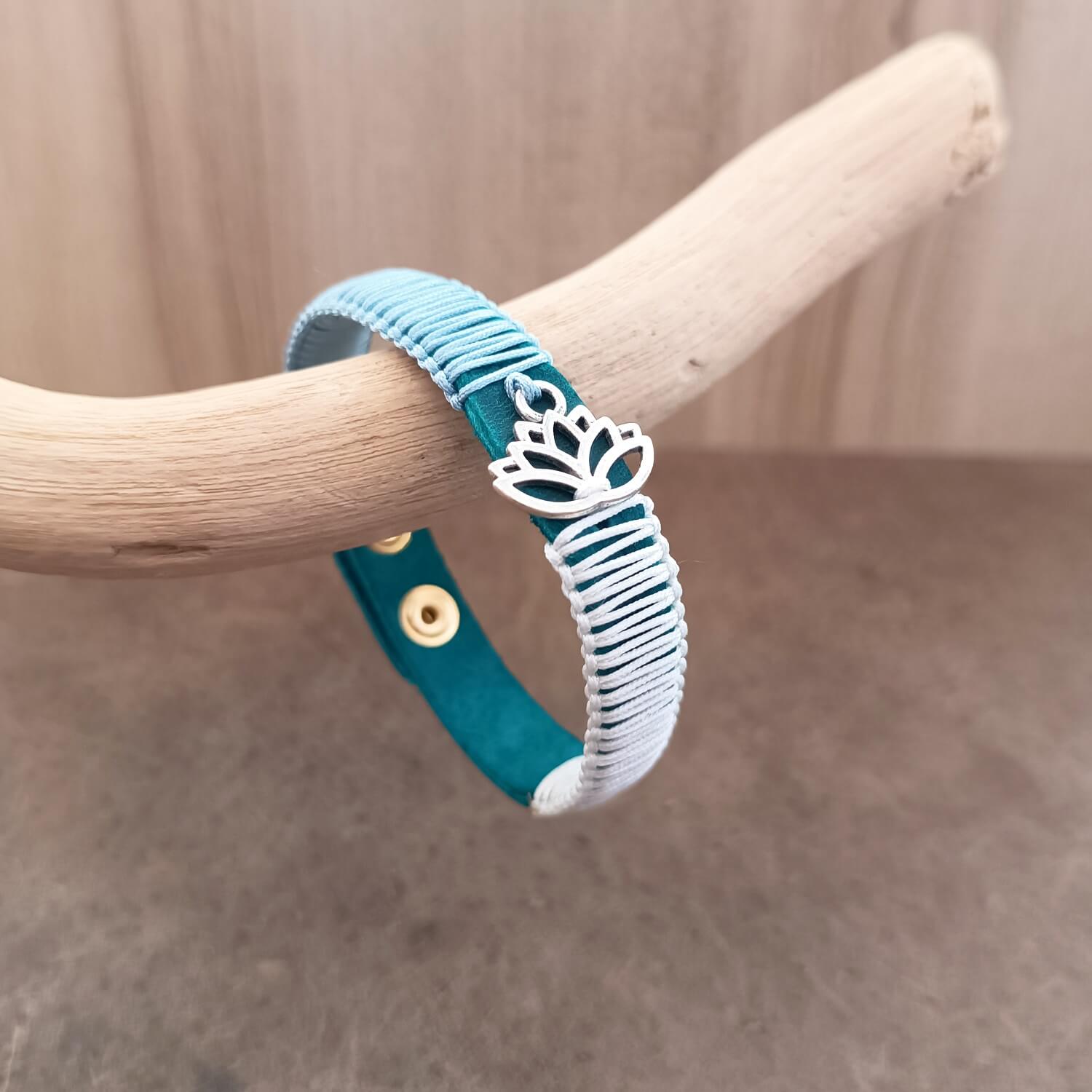 Close-up of The Lotus's Serenity Bracelet, highlighting the intricate details of the polished stainless steel lotus flower pendant and the texture of the macrame cords against the blue leather.