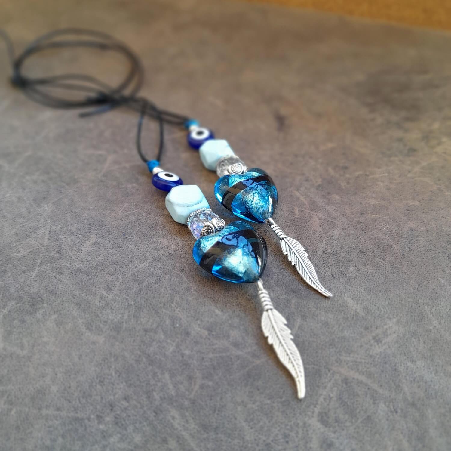 Detailed close-up of the natural, irregular turquoise stone, silver heart, feather, and evil eye on the charm, highlighting their unique shapes and textures.