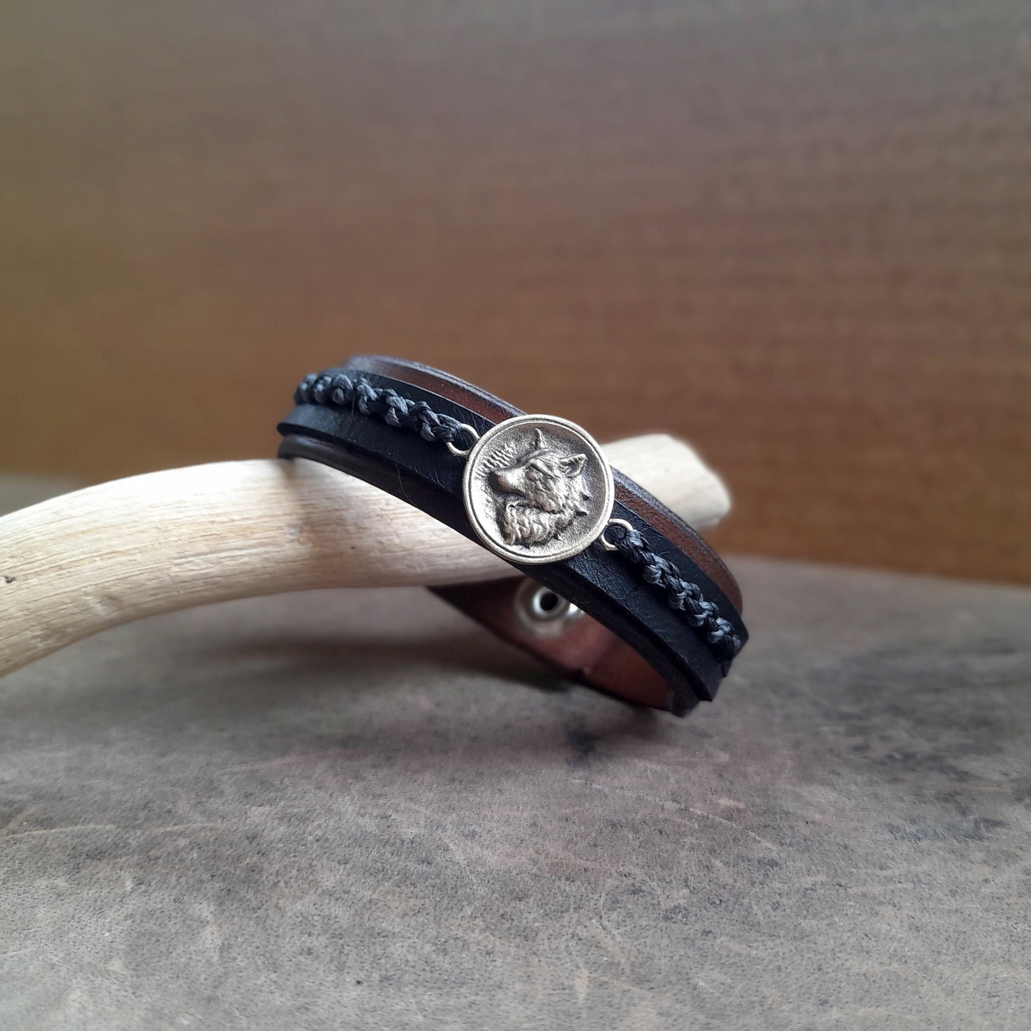 Close-up of the Great Nordic Wolf Leather Bracelet, highlighting the intricate details of the oxidized brass wolf pendant against the textured leather, with the industrial gray and black waxed cord braid.