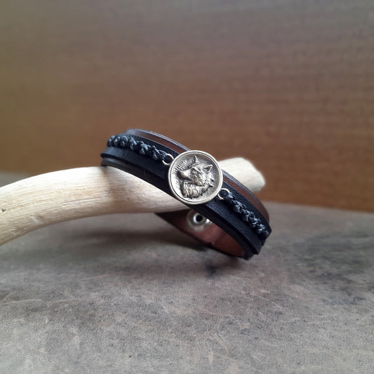 Close-up of the Great Nordic Wolf Leather Bracelet, highlighting the intricate details of the oxidized brass wolf pendant against the textured leather, with the industrial gray and black waxed cord braid.