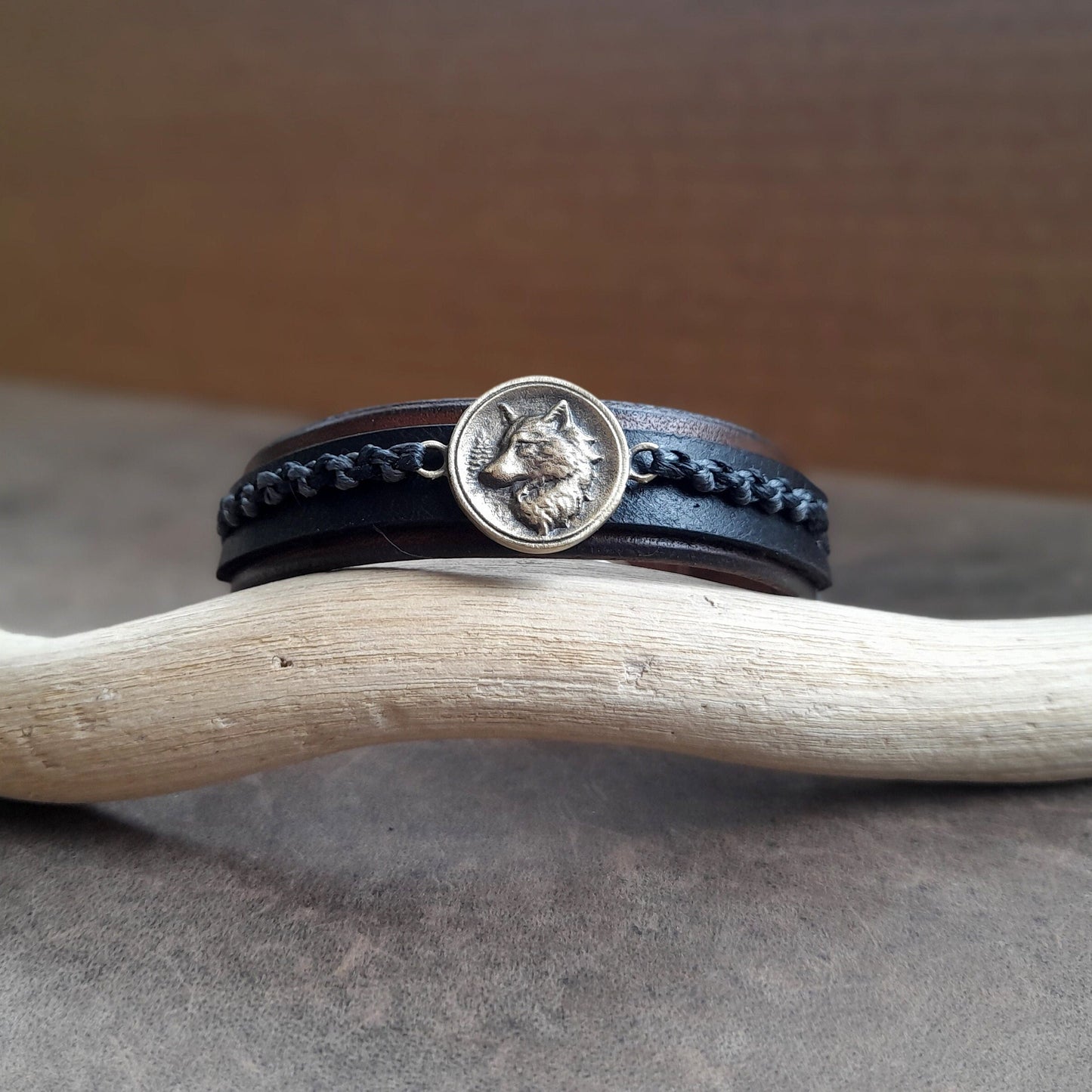 Close-up of the Great Nordic Wolf Leather Bracelet, highlighting the intricate details of the oxidized brass wolf pendant against the textured leather, with the industrial gray and black waxed cord braid.