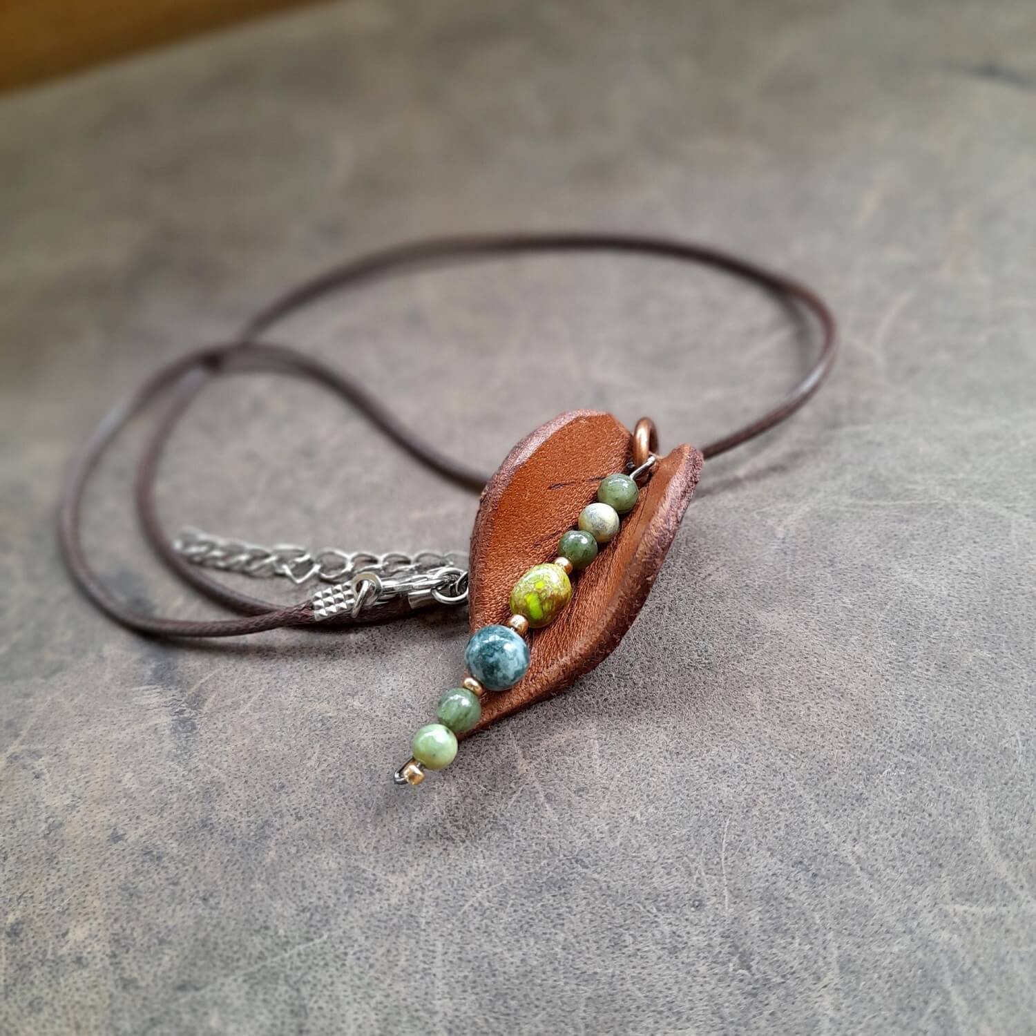 Necklace with a brown leather leaf pendant and green beads on a gray surface
