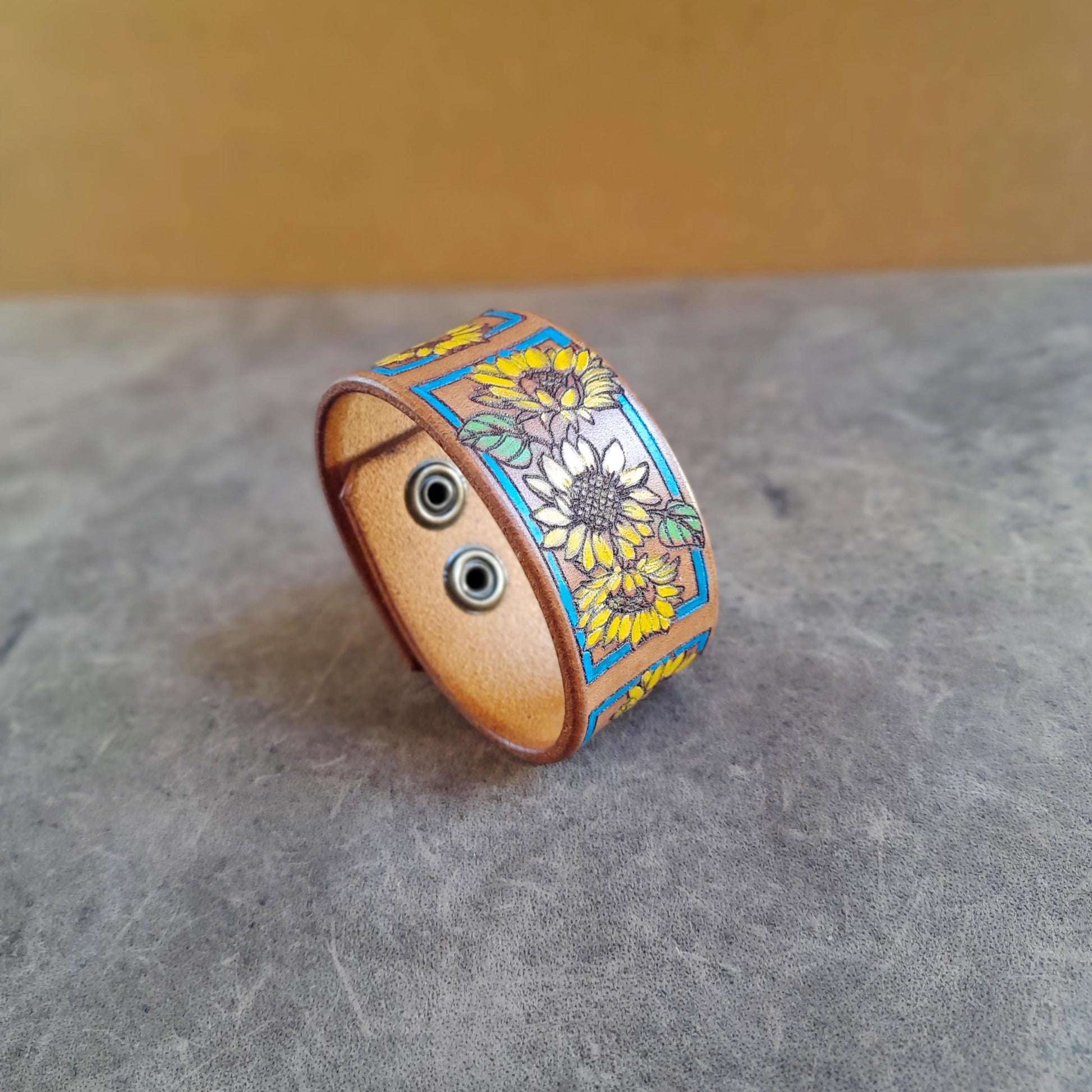 Close-up side view of The Sunshine Bloom Leather Cuff Bracelet, highlighting the texture of the mustard brown Crazy Horse leather and the intricate laser-engraved outlines of the hand-painted sunflowers.