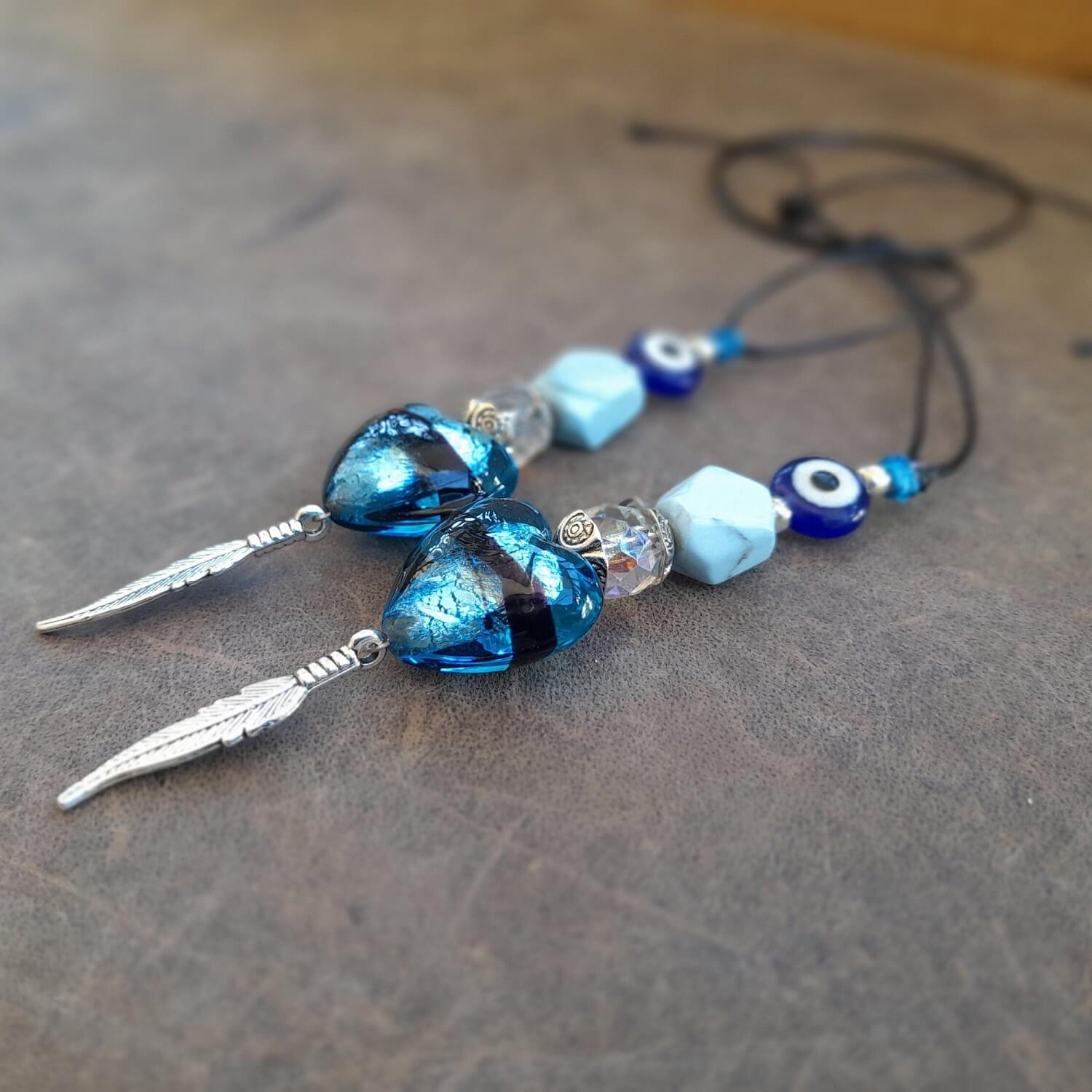 Close-up side view of Turquoise Stone & Silver Elements:Detailed close-up of the natural, irregular turquoise stone, silver heart, feather, and evil eye on the charm, highlighting their unique shapes and textures.