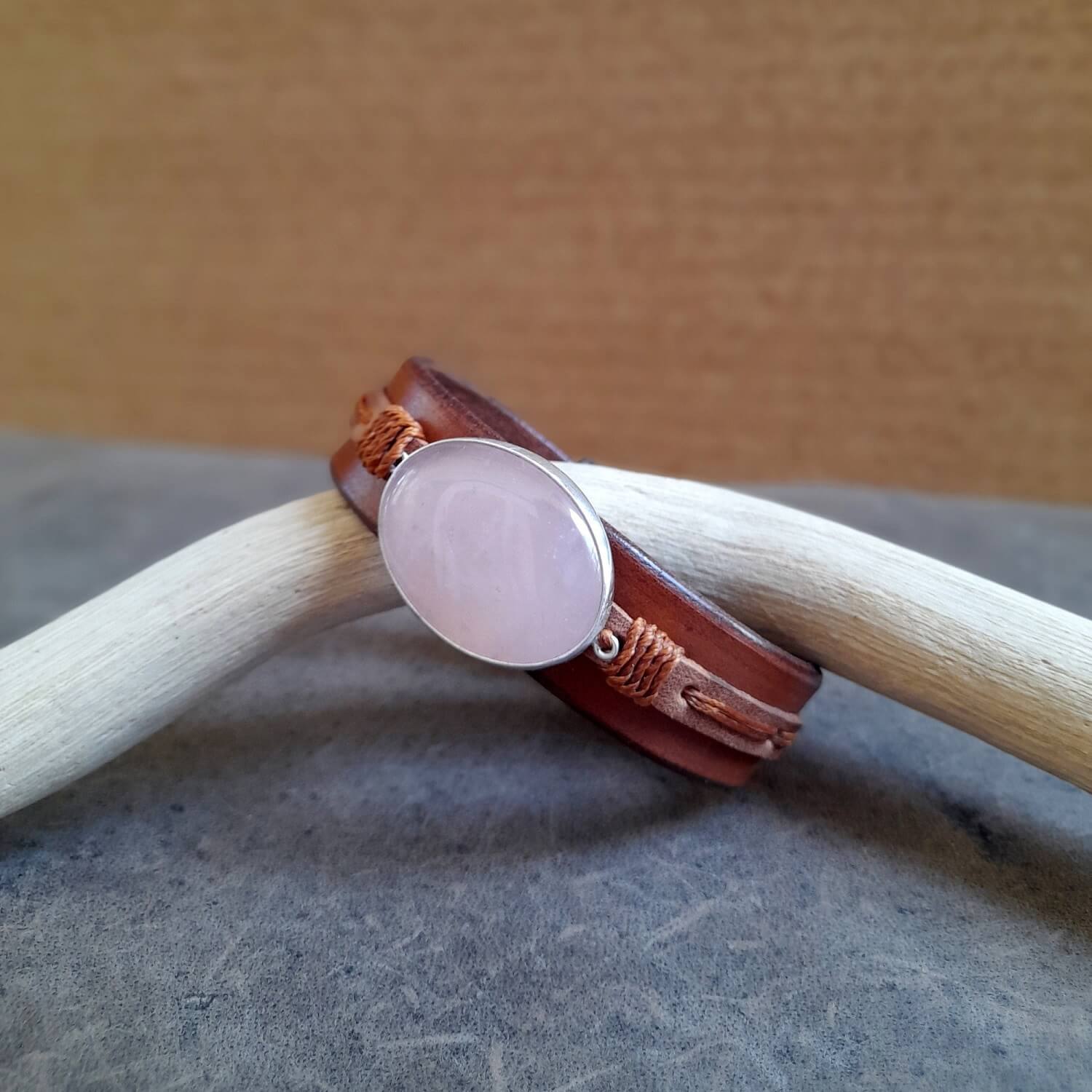 Close-up showing the wide oiled Vachetta leather bottom band and the brown cowhide top layer on the cuff, with the warm brown waxed cord wrapping the pendant.
