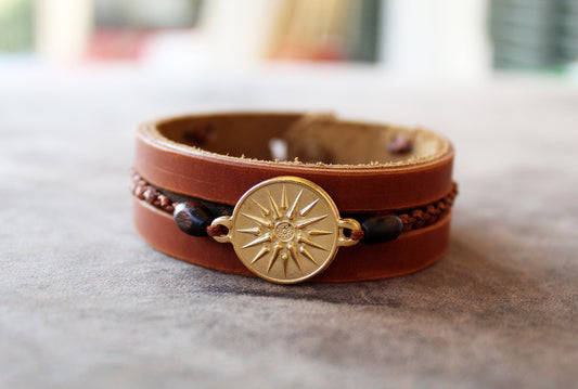 Close up of Gold Vergina Sun Leather Bracelet with gold-plated Vergina Sun & Alexander the Great charm on flat surface. Features brown leather, wooden beads, and macrame.