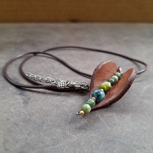 Hand-shaped leather leaf pendant necklace with Moss Agate and Green Jasper beads, on a dark background.