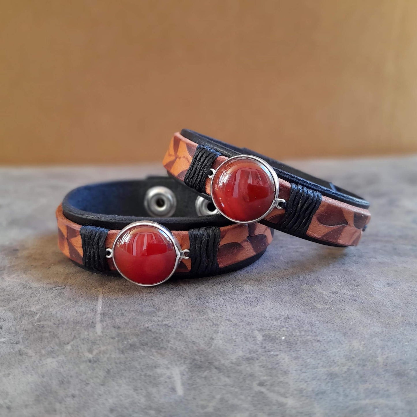 Close up of Two Ember Bloom Cuffs displayed side-by-side, showcasing them as a matching pair. Both bracelets feature hand-pyrographed leather and Red Carnelian in sterling silver pendants.
