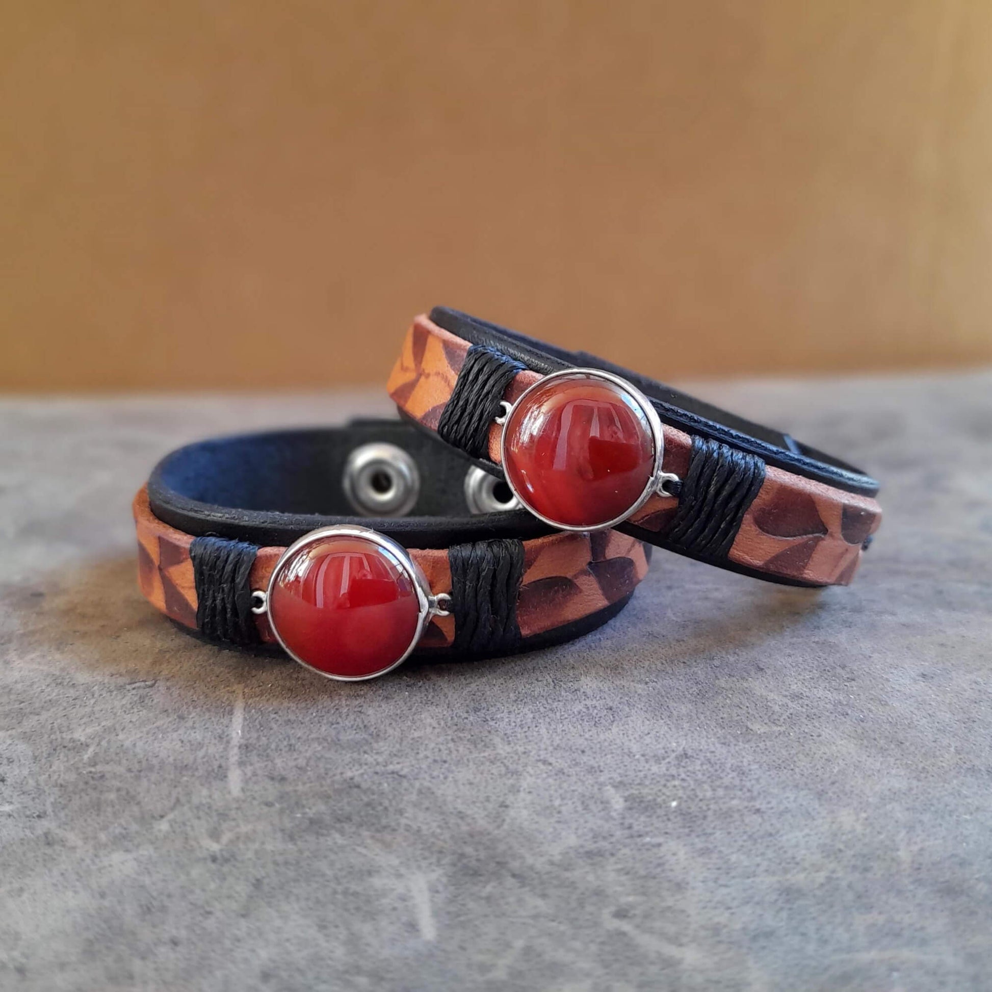 Close up of Two Ember Bloom Cuffs displayed side-by-side, showcasing them as a matching pair. Both bracelets feature hand-pyrographed leather and Red Carnelian in sterling silver pendants.