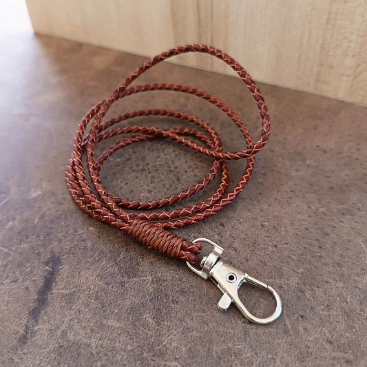 Brown braided leather lanyard with metal clip on a stone surface
