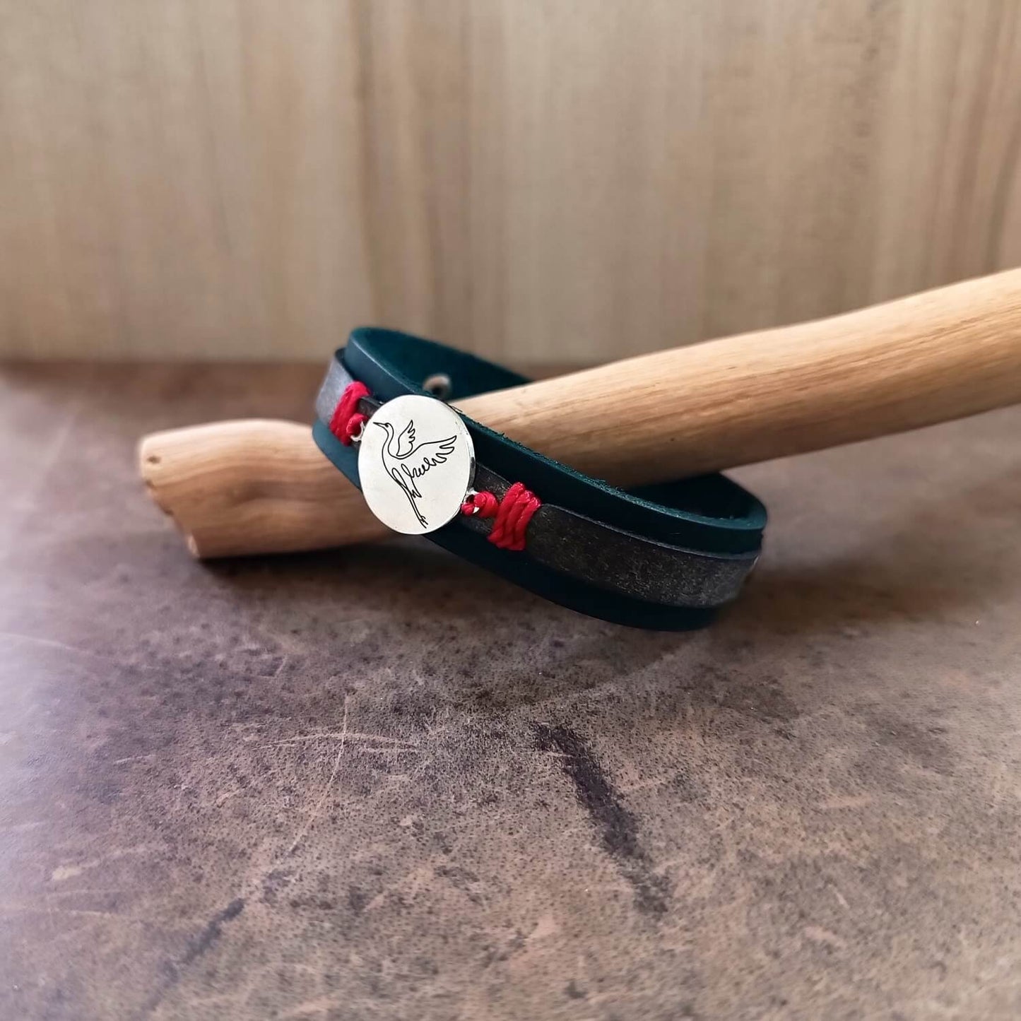 Indigo leather bracelet with red accents and Crane pendant on a wooden stick against a neutral background