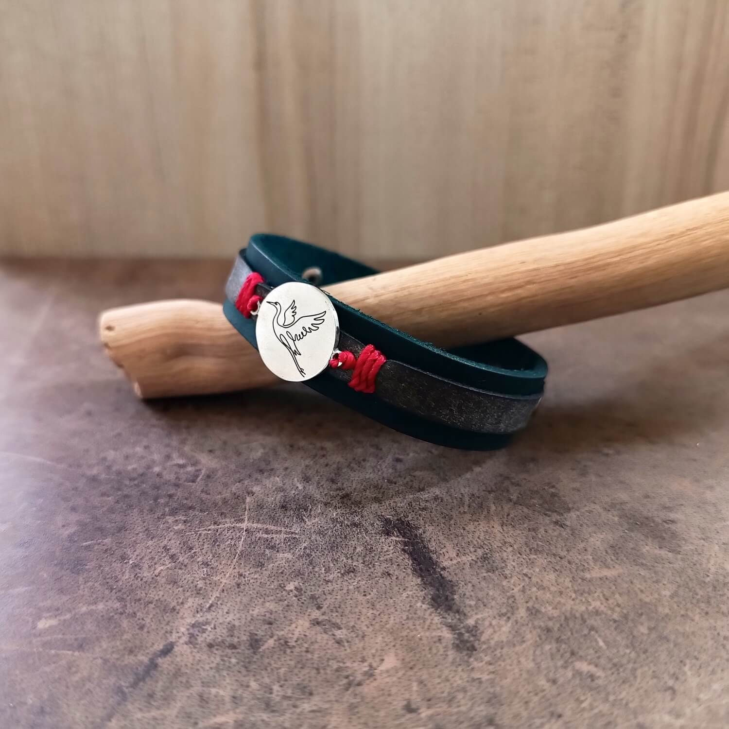 Indigo leather bracelet with red accents and Crane pendant on a wooden stick against a neutral background