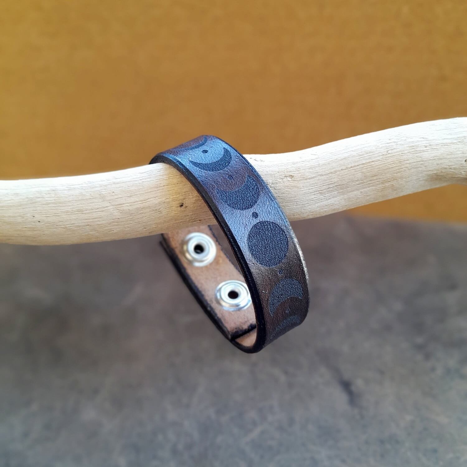 Brown leather bracelet with laser engraved moon cycle hanging from a driftwood