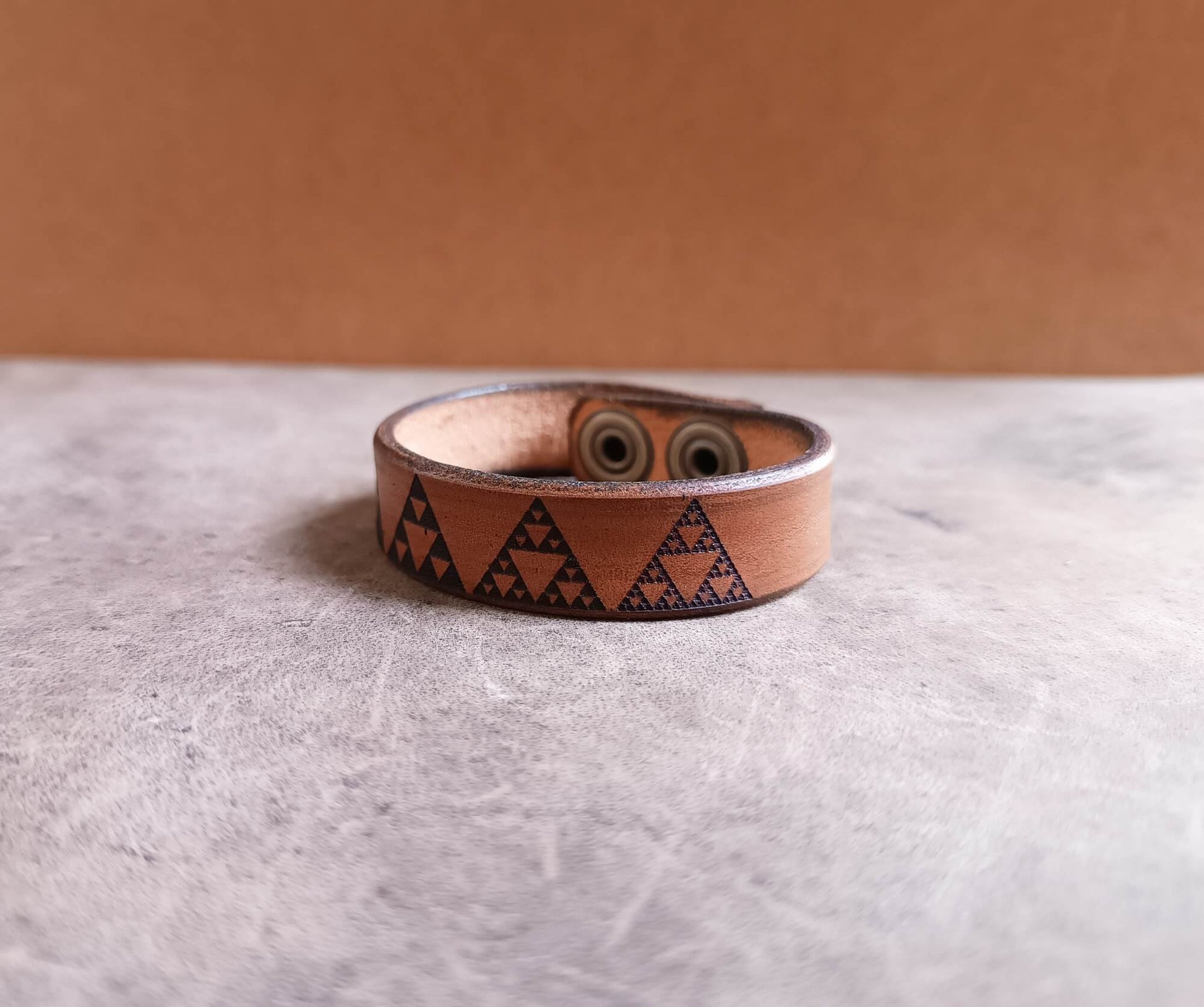Brown leather bracelet with geometric pattern on a light gray surface