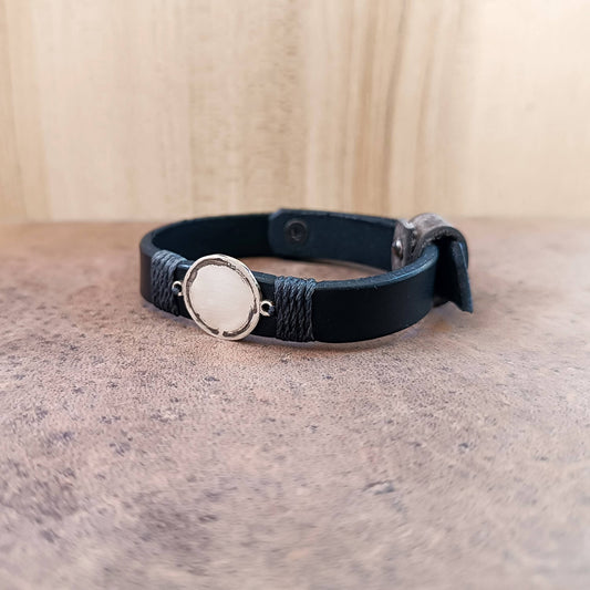 Black leather bracelet with a silver Enso circle pendant on a textured surface