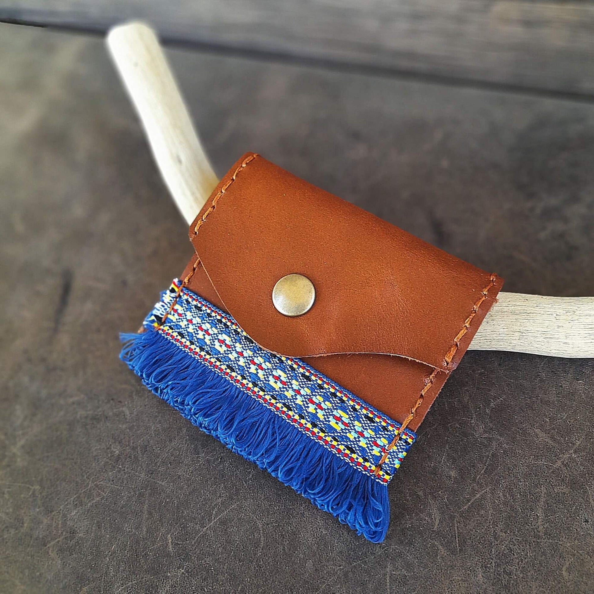 Brown leather wallet with blue fringes on a wooden stick