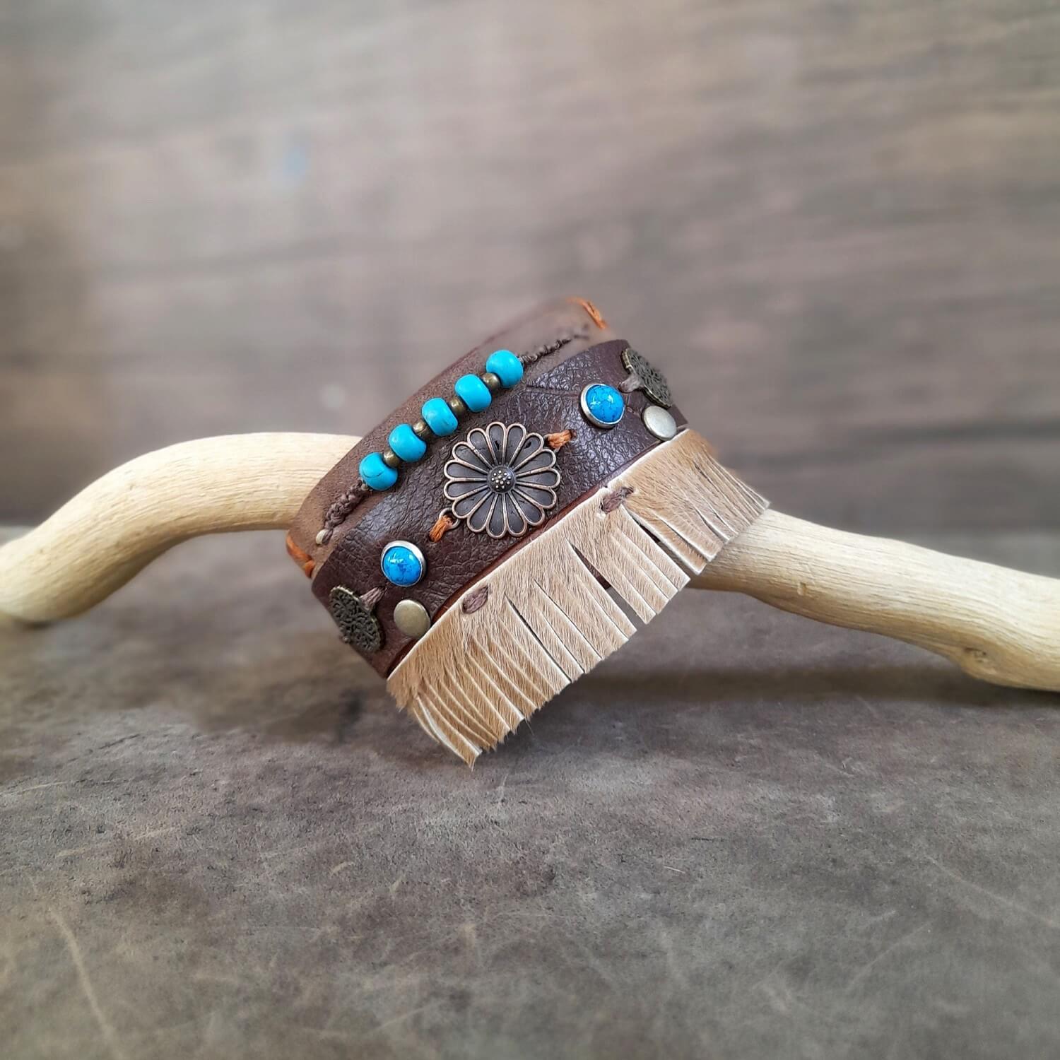 Extra wide chunky boho leather cuff in brown with antique bronze floral charms, turquoise rivets, macrame, and hair on hide fringe.