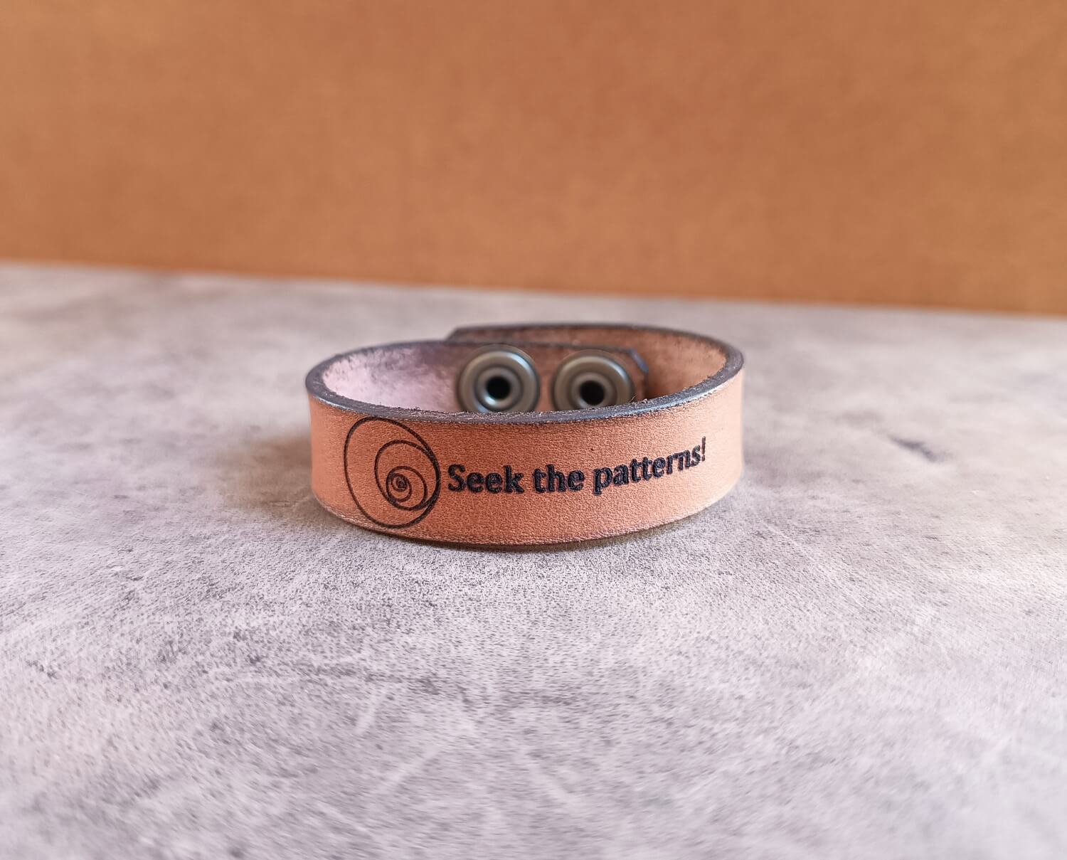 Brown leather bracelet with fibonacci sequence and text on a gray surface