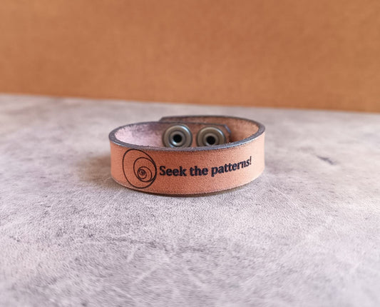 Brown leather bracelet with fibonacci sequence and text on a gray surface