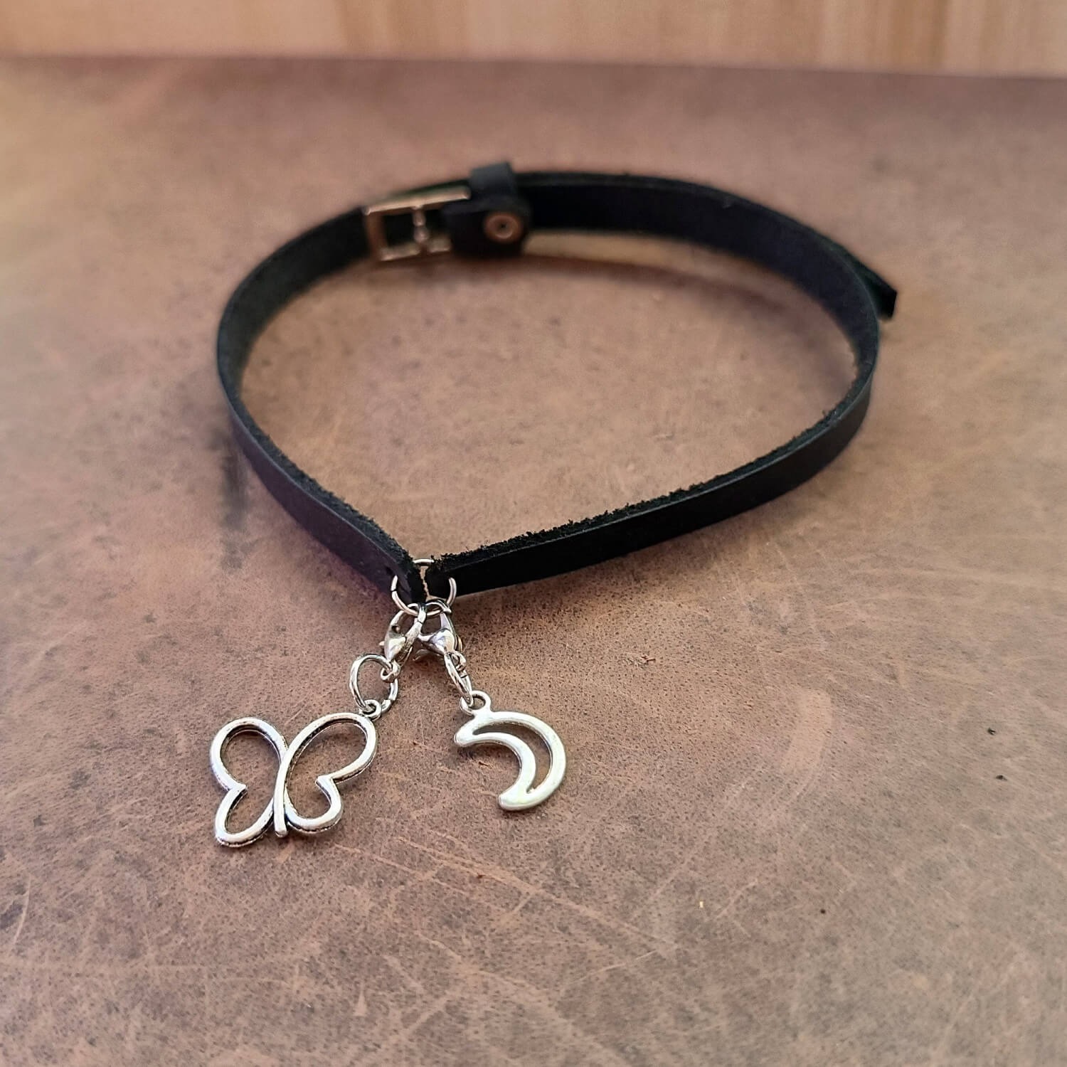 Black choker necklace with butterfly and crescent moon charms on a wooden surface