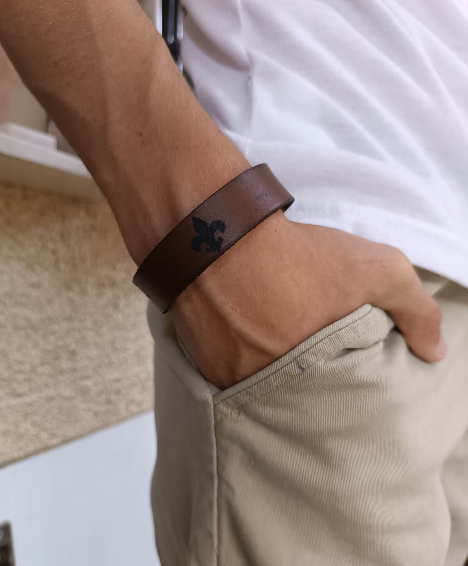 Brown leather bracelet with a Fleur de Lis worn on a wrist, with a blurred background.
