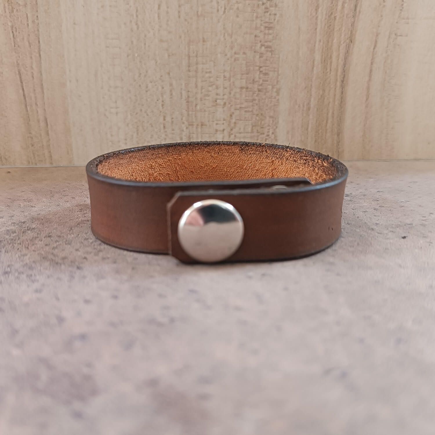 Brown leather bracelet with a silver button on a neutral background