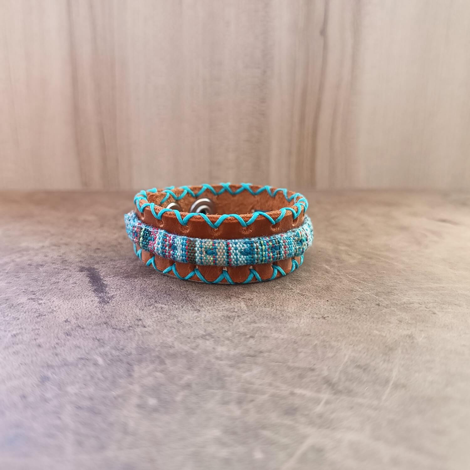 Front view of handmade unisex boho leather bracelet with tribal embroidered cord and snap button closure