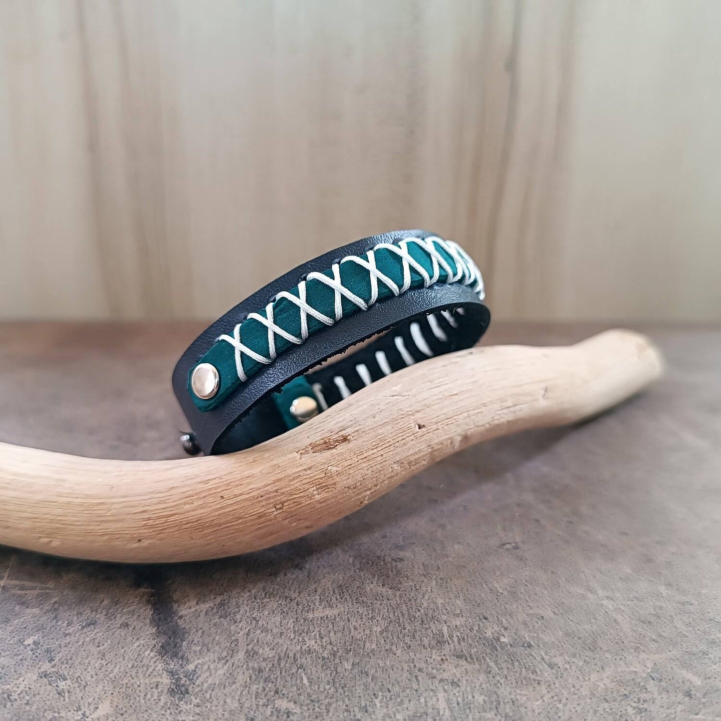 Teal leather bracelet with white stitching on a wooden branch