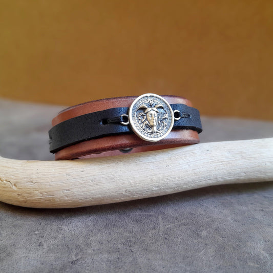 Greek Medusa Leather Bracelet on flat surface, showing handcrafted oxidized brass Medusa charm, brown Crazy Horse leather, and black stripe.