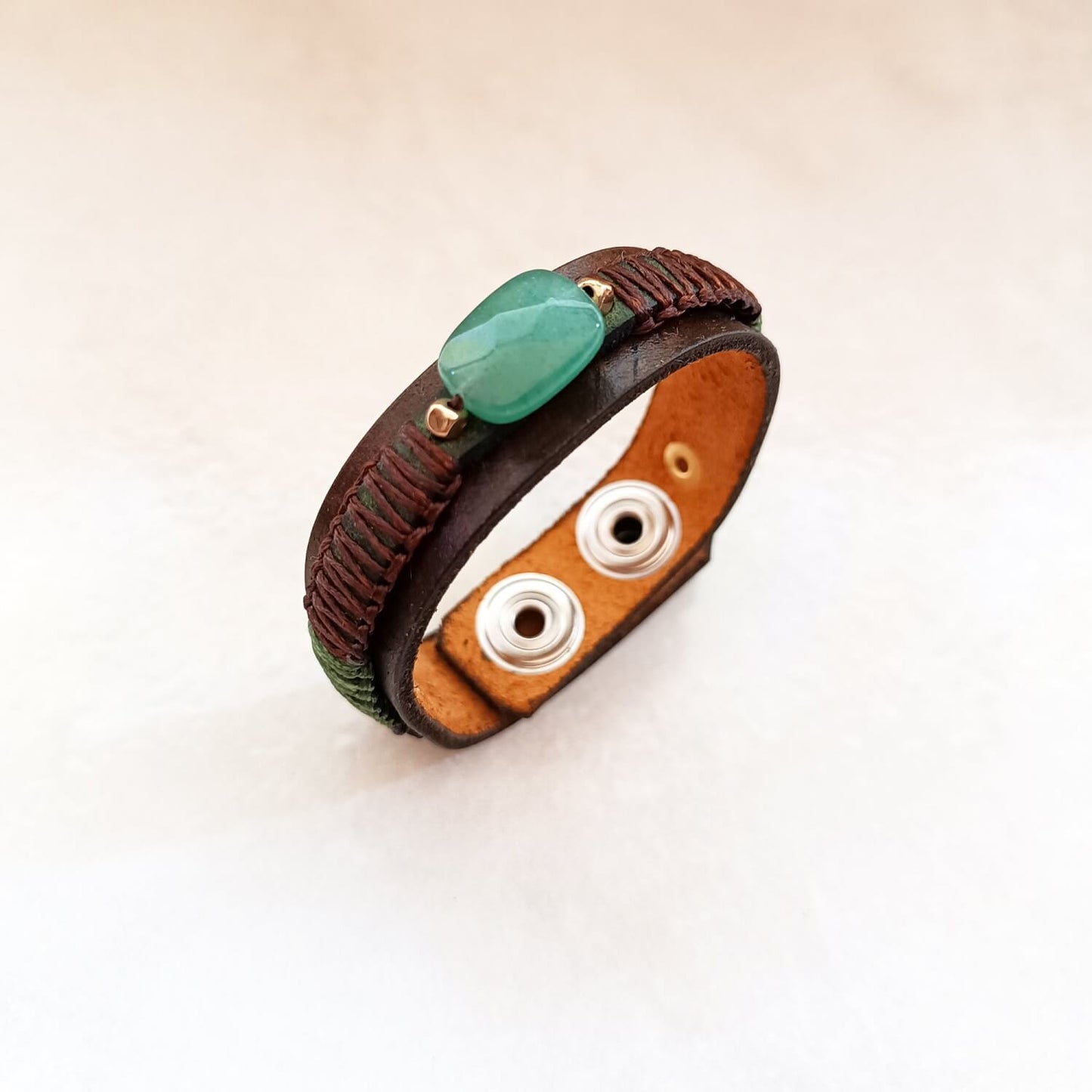 Brown leather bracelet with a large green Aventurine stone and metal beads on a marble