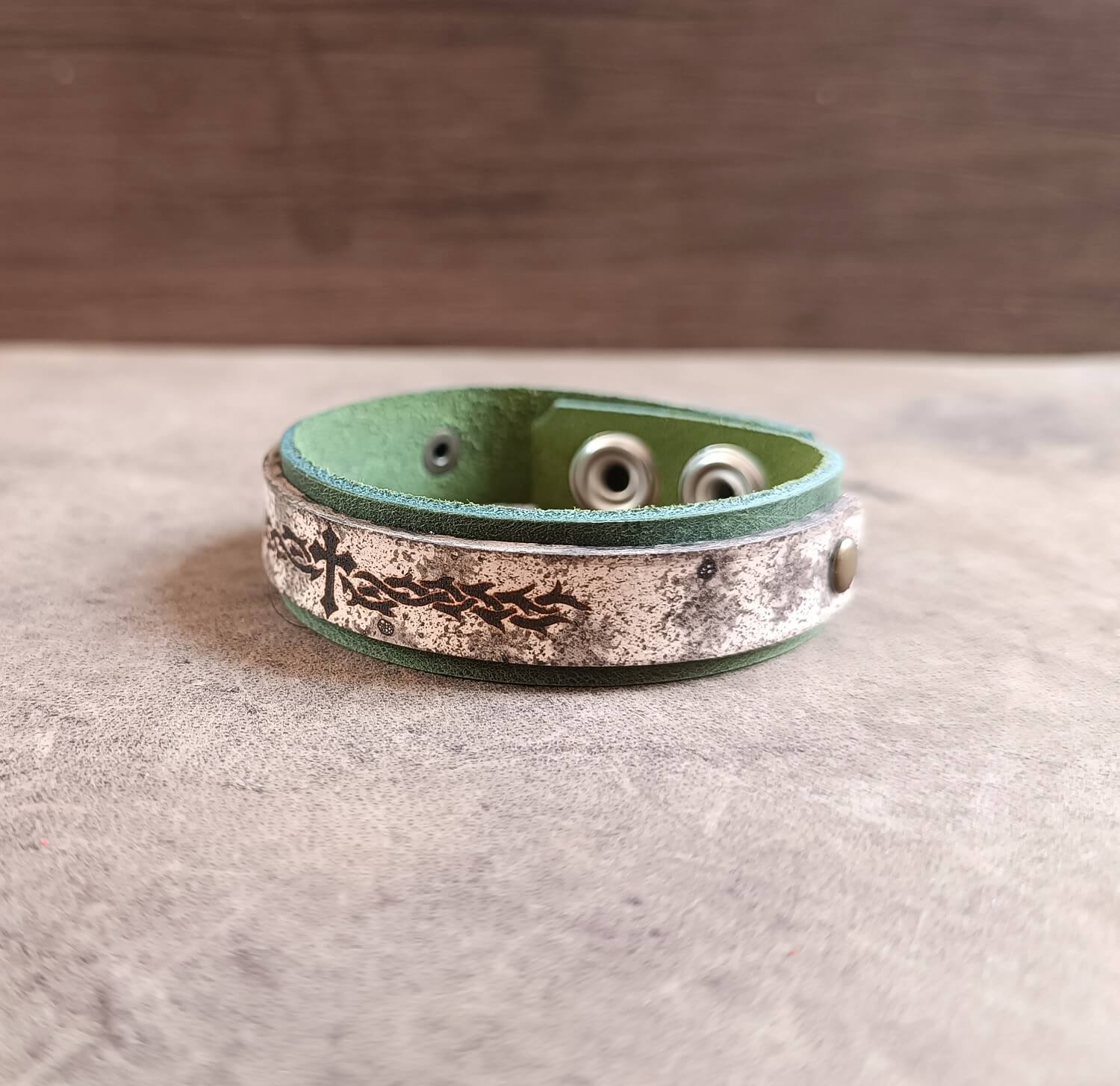 Green leather bracelet with metallic band on a wooden surface