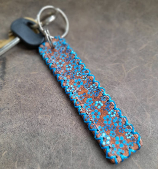 The Hand Painted Forget Me Not Personalized Leather Keychain: A brown Crazy Horse leather keychain featuring delicate hand-painted forget-me-not flowers, blue hand-stitching, and two split rings.