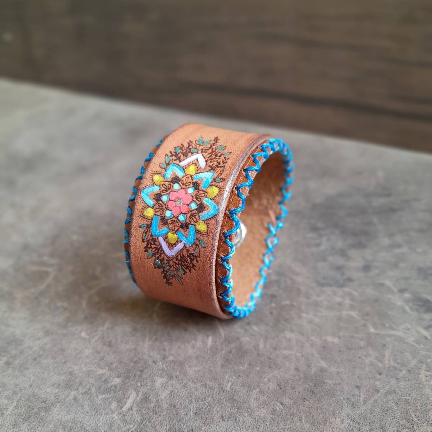 The Hand Painted Mandala Flower Leather Bracelet: A brown layered leather bracelet featuring a cheerful hand-painted mandala flower design with turquoise hand-stitching.