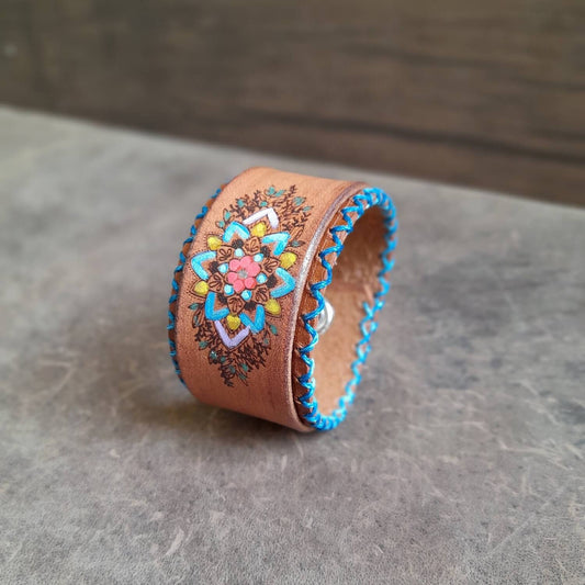 The Hand Painted Mandala Flower Leather Bracelet: A brown layered leather bracelet featuring a cheerful hand-painted mandala flower design with turquoise hand-stitching.